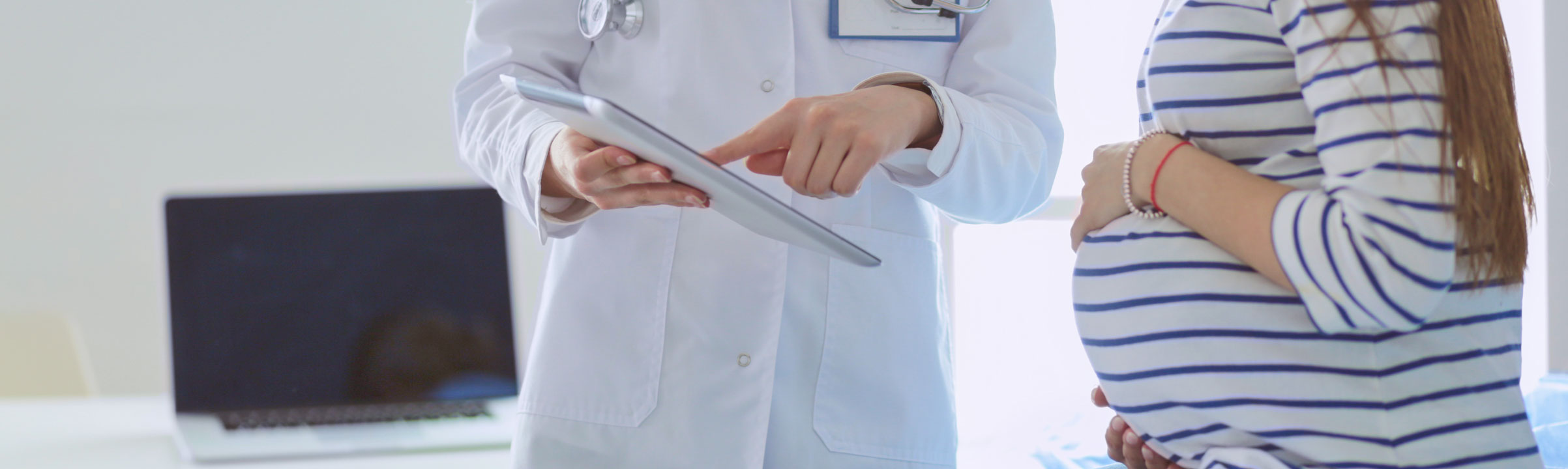 Das Bild zeigt eine Ärztin, die einer schwangeren Patientin etwas auf einem Tablet erklärt.